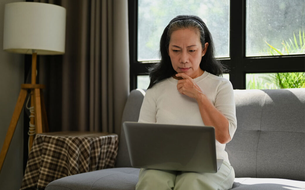An older woman contemplating while looking at a laptop at home.