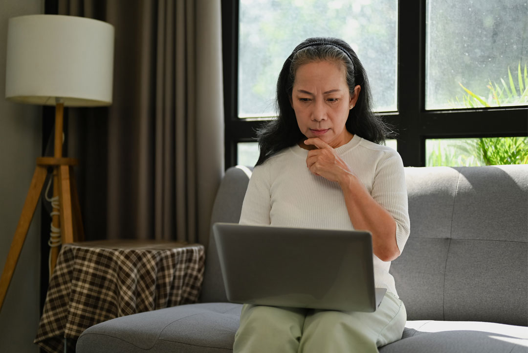 An older woman contemplating while looking at a laptop at home.